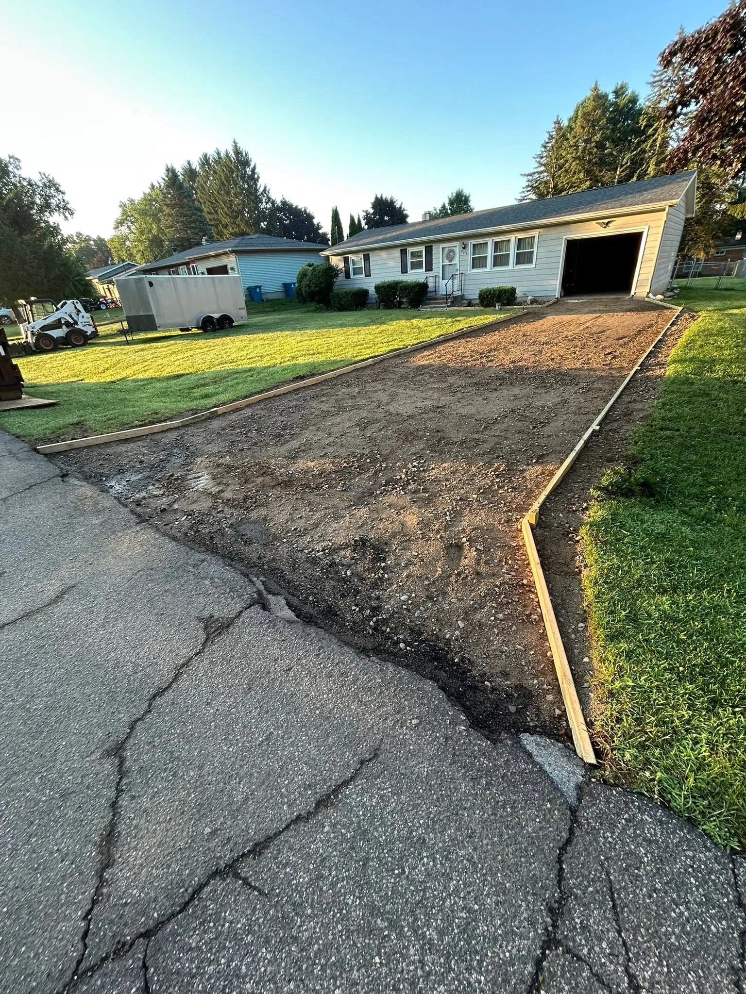 The driveway mid-job with the old surface removed, showing the excavated gravel base and timber forms set along both edges.