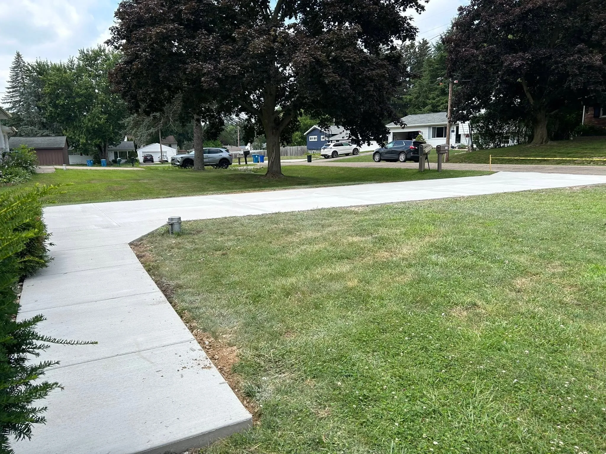 A finished concrete driveway and separate front walk, cured and clean, edged against the lawn of a residential street.