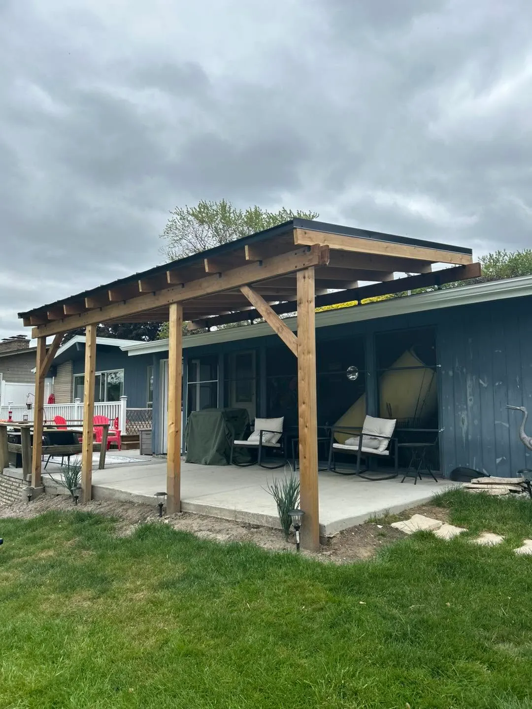 A cedar patio cover with exposed rafters and a dark metal roof, built by Built By Williams over a poured concrete patio.