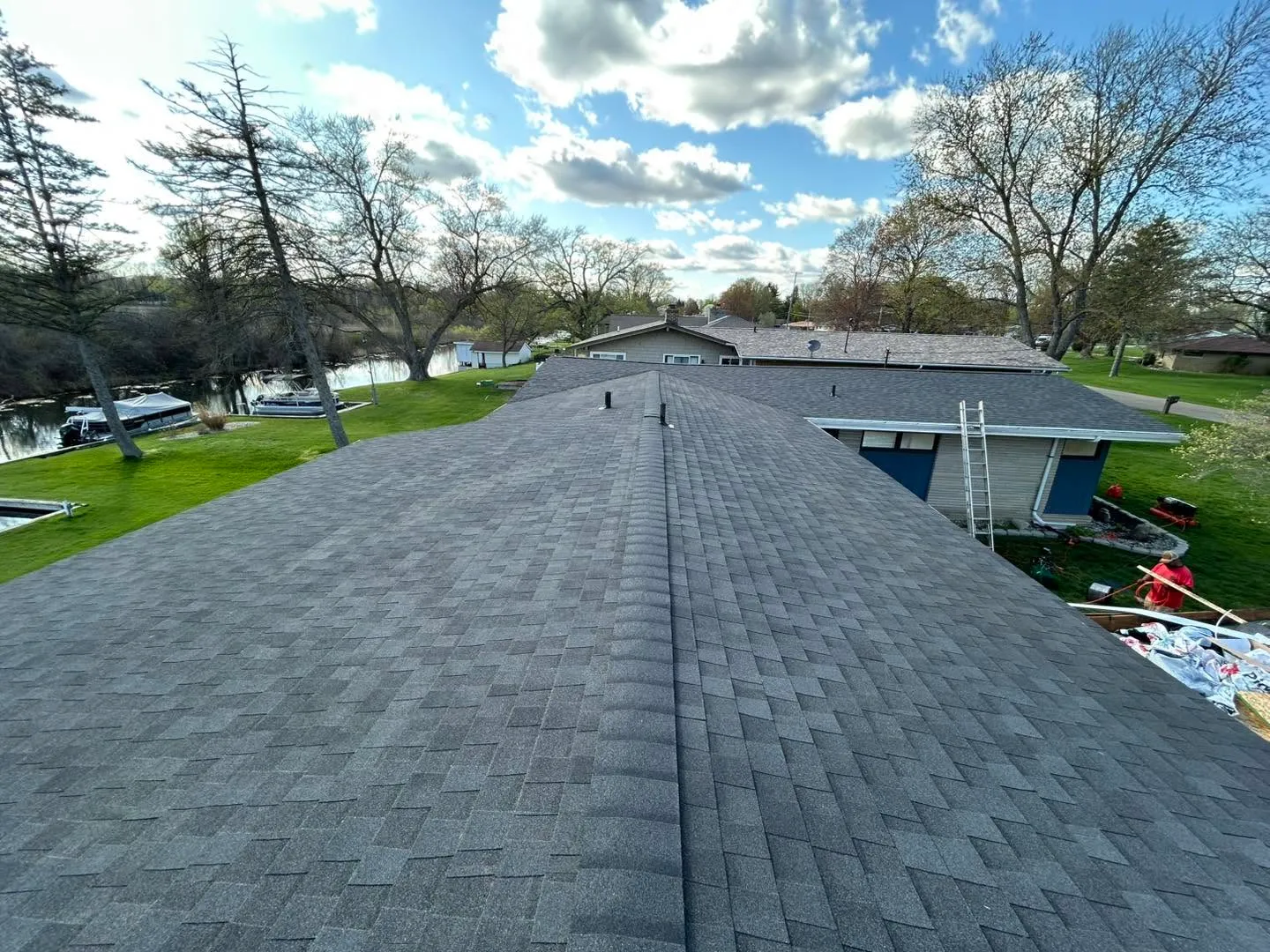 A completed architectural shingle roof photographed from the ridge, with a lake and docked pontoon boats beyond.